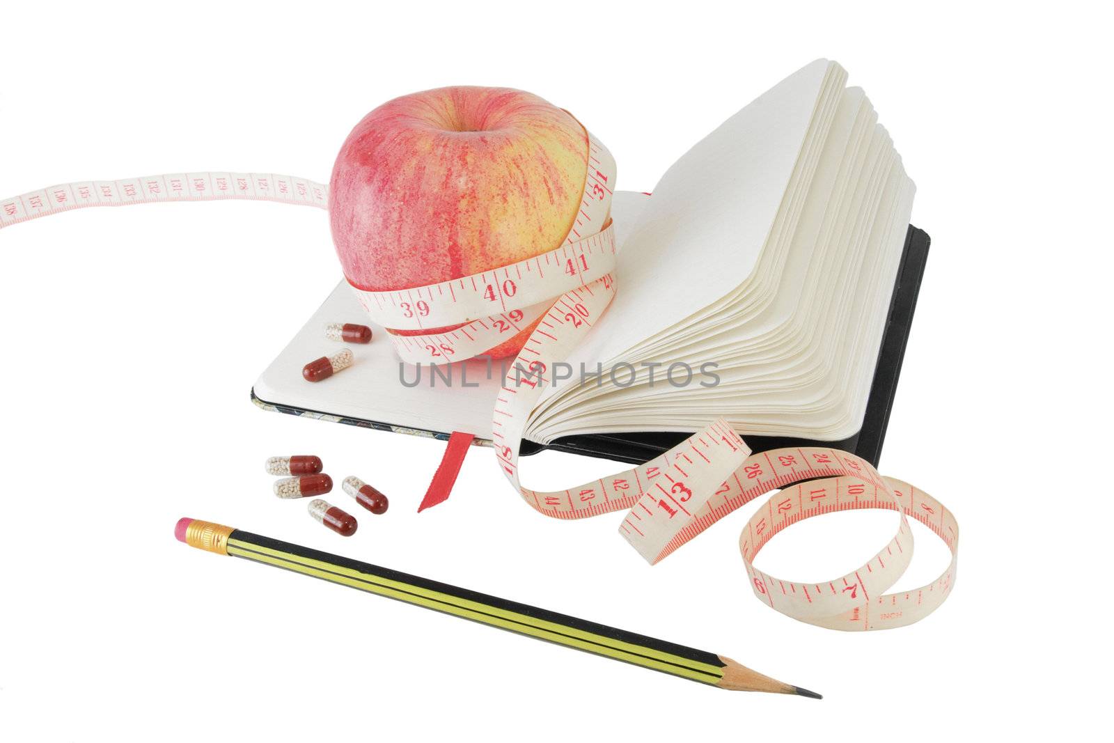 Copybook with apple, measure tape and vitamin pills to aid effective diet