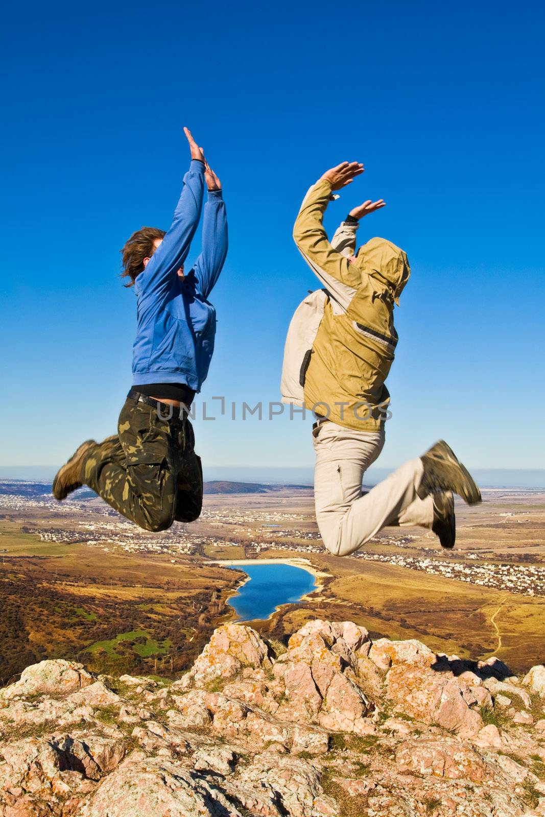 Two hikers jumping cheerfully on mountain summit in clear sunny weather