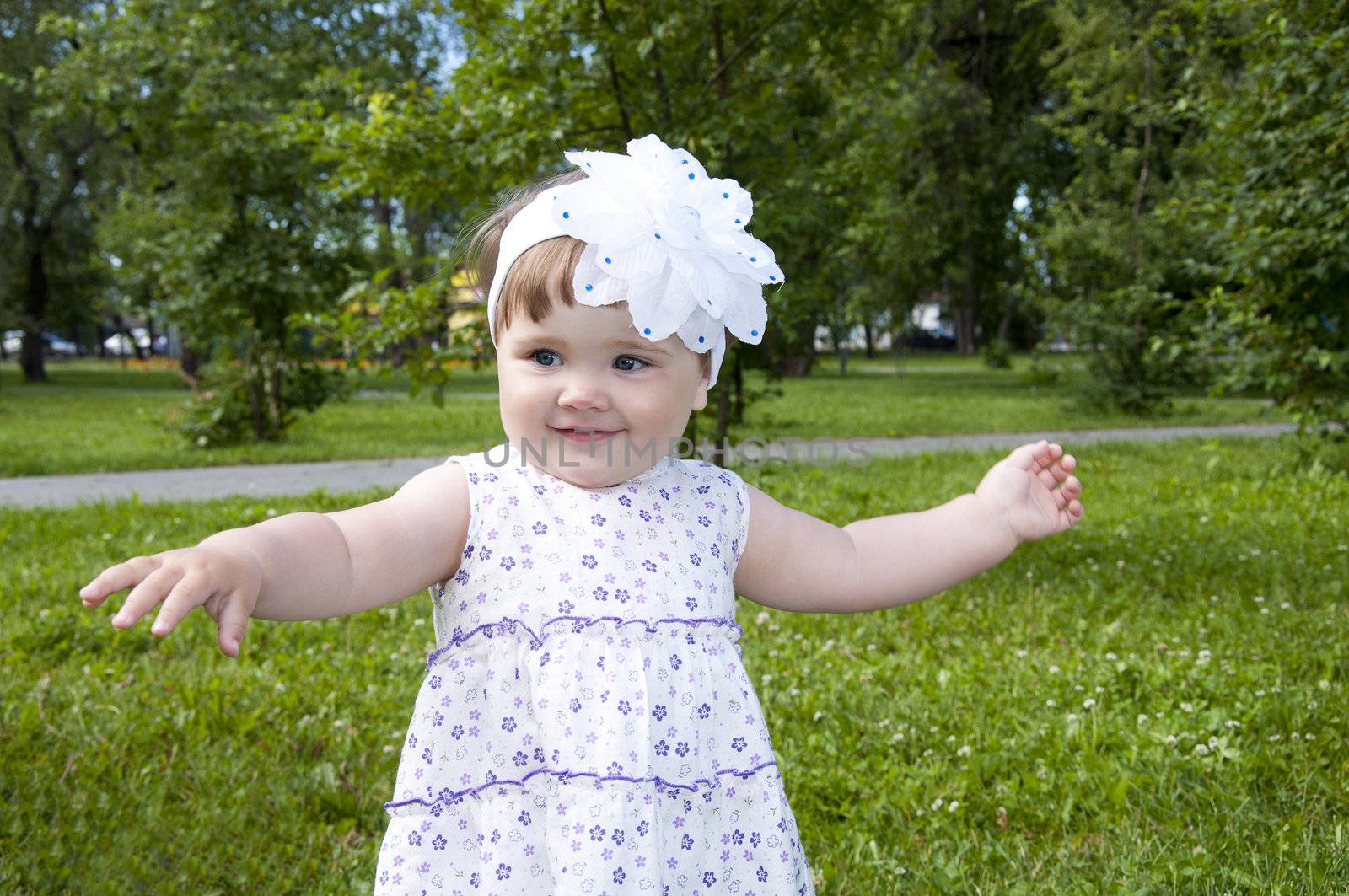 cute little girl dancing in the park, background green grass and trees