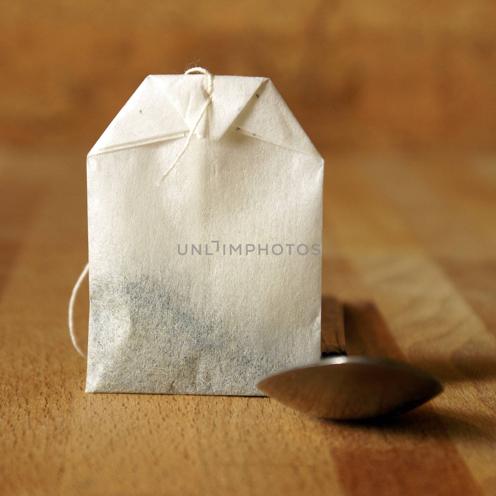 A square format shot of a tea bag and spoon for preparing the beverage.