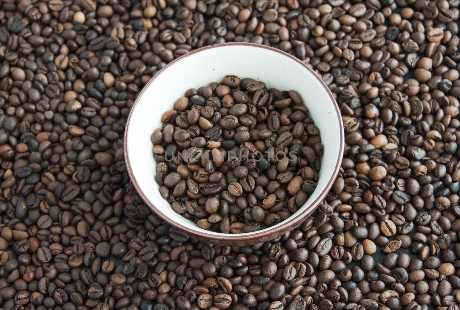A cup full of coffee beans, surrounded by other coffee beans