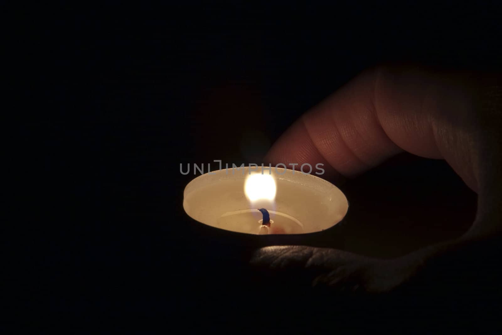 Male hand holding a little candle in darkness