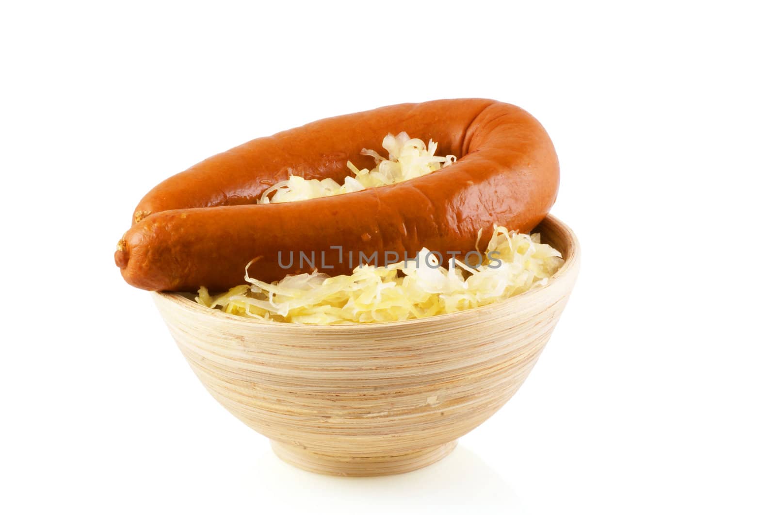 Wooden bowl with sauerkraut and a smoked sausage on a white background.              