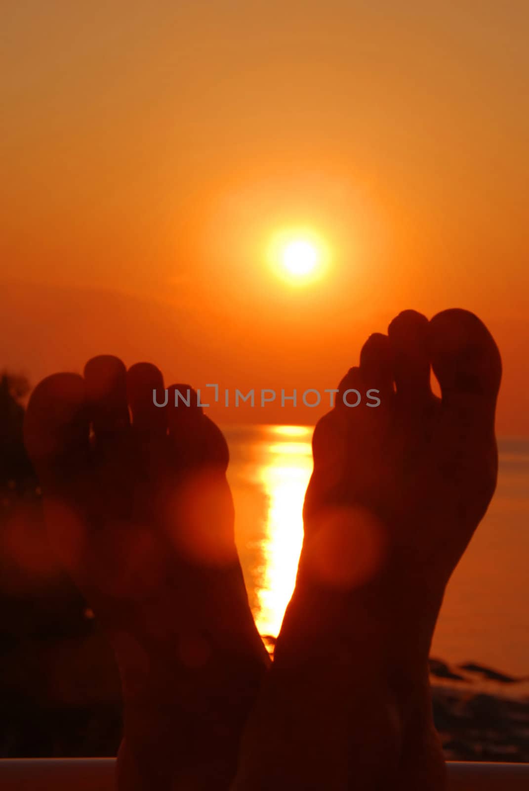 orange sun rising above a sea over crossed feet