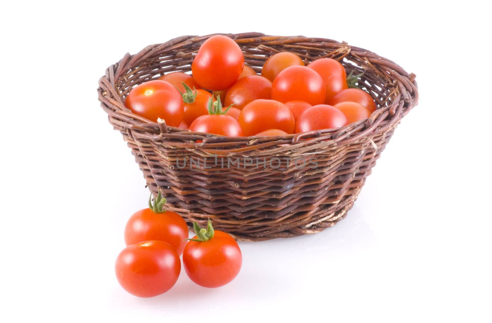 Basket full of tomatoes, with a few next to it, isolated on white.