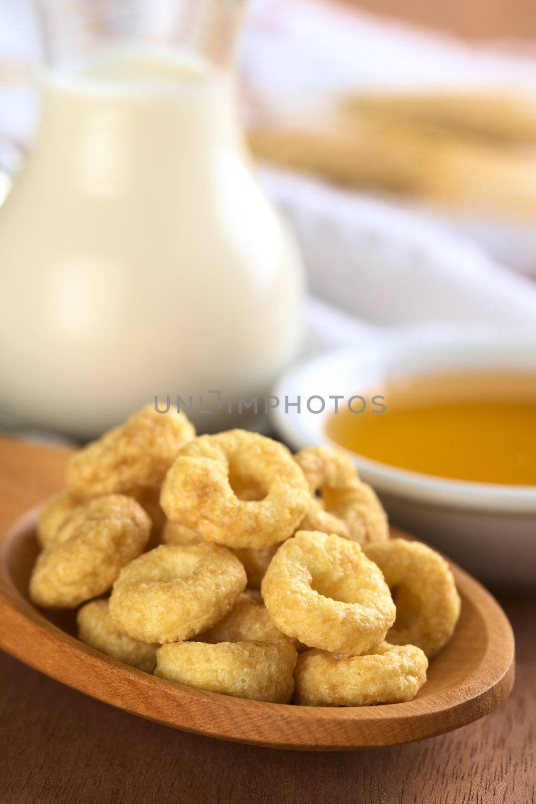 Honey flavoured cereal loops on wooden spoon with milk and honey in the back (Selective Focus, Focus on the front of the loops in the front)