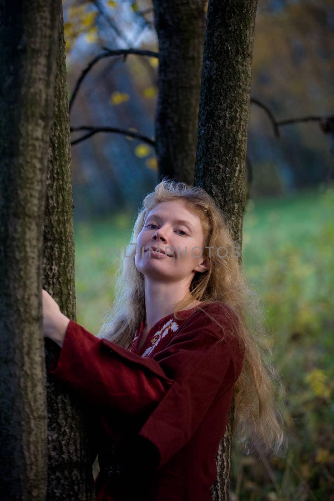 The blonde girl in medieval red dress in the autumn forest
