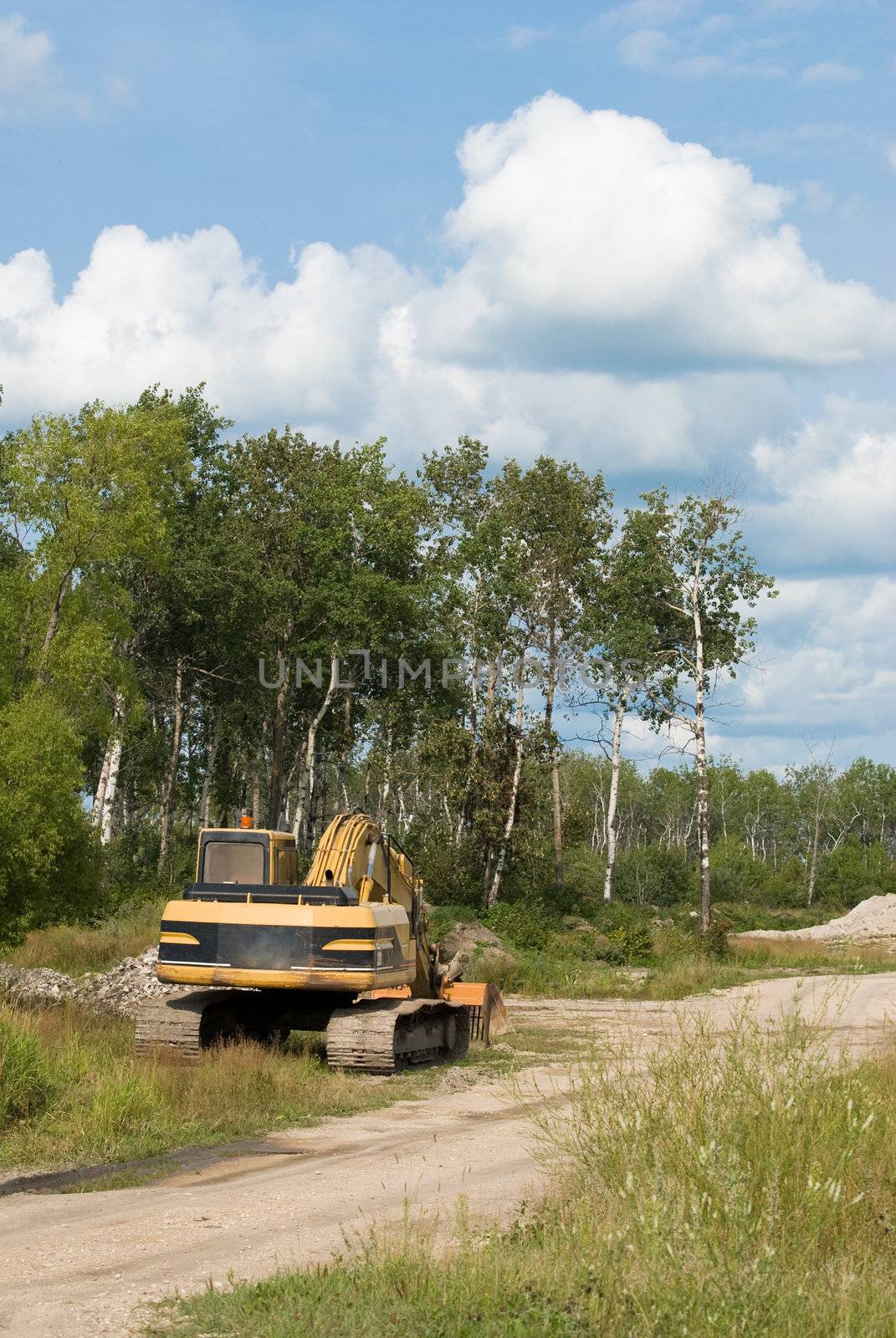 An excavator parked on the side of a gravel road near a job site