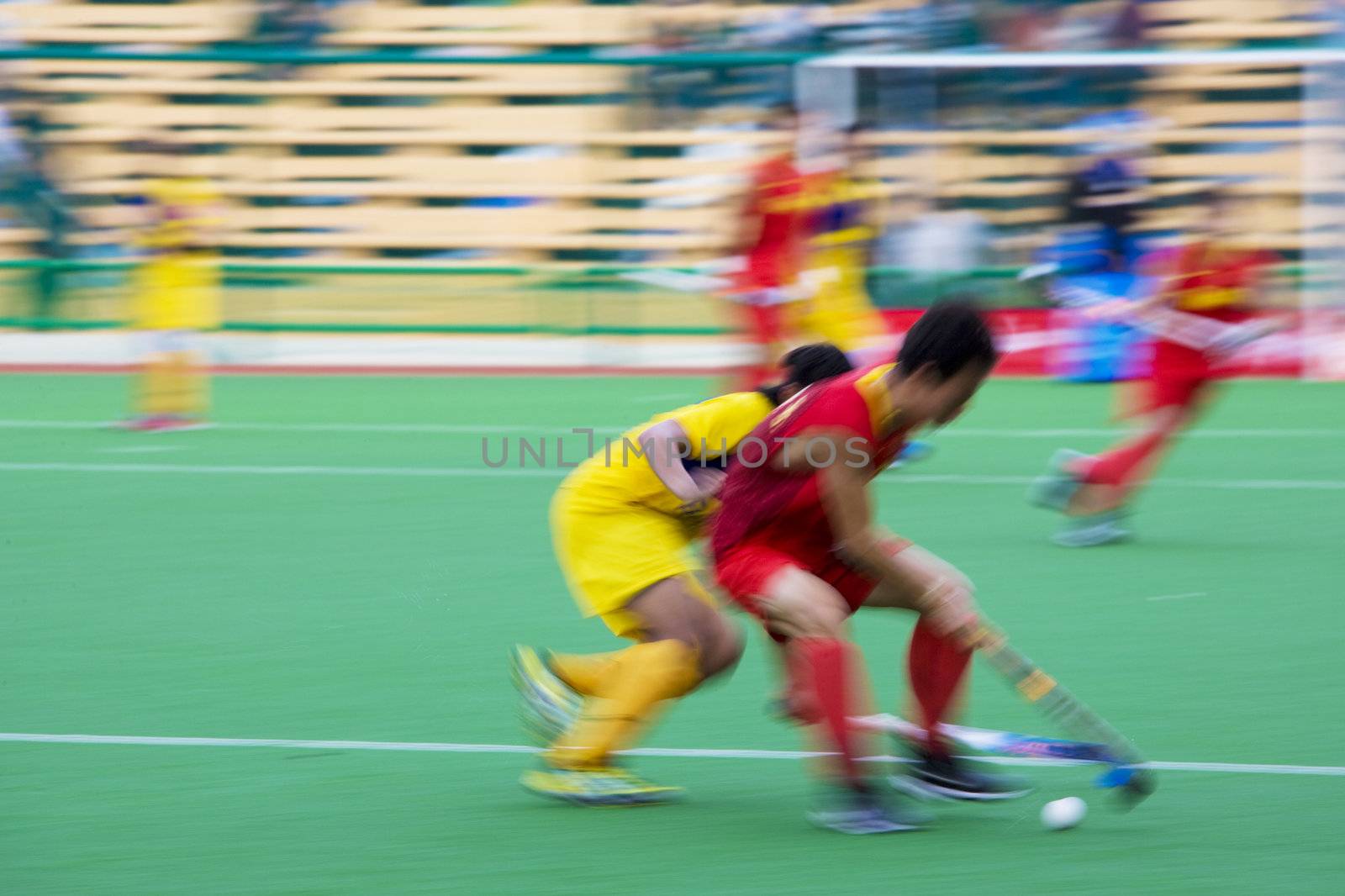 Image of men's field hockey players in action. Image intentionally blurred to portray speed.