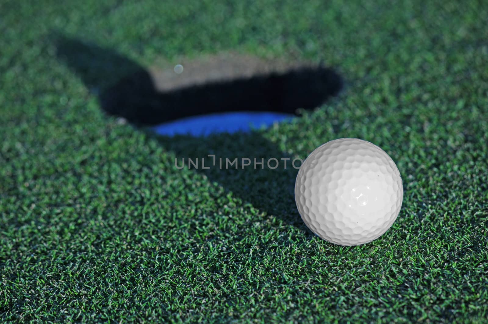 golf ball shadow skimming edge of cup on green
