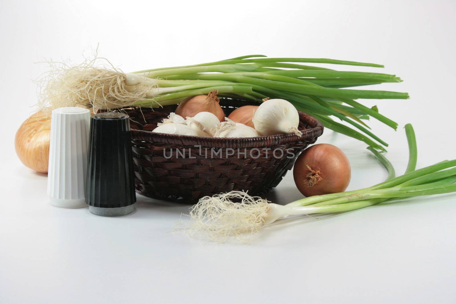 Onions napiform white and usual, and also green in a basket with salt and pepper.