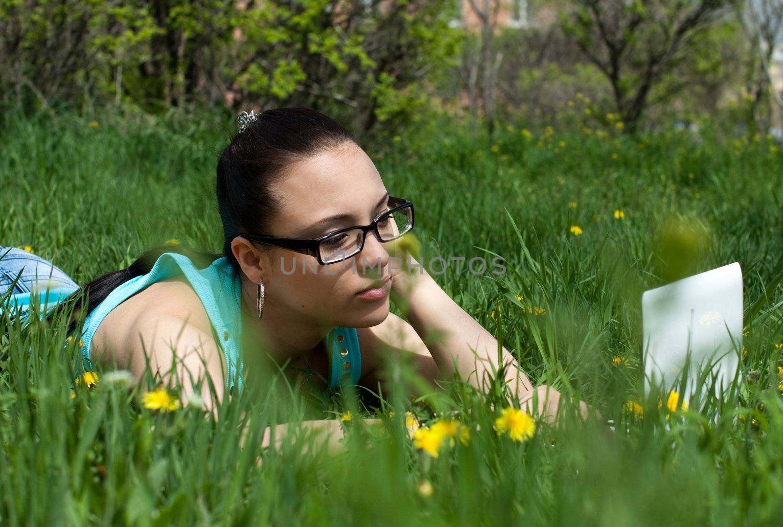 Photo of a girl with a laptop, on a background of flowers and green grass