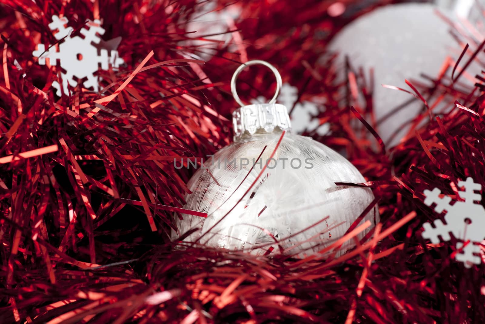 Silver christmas ball ornament sitting in red garland with silver snowflake shapes.