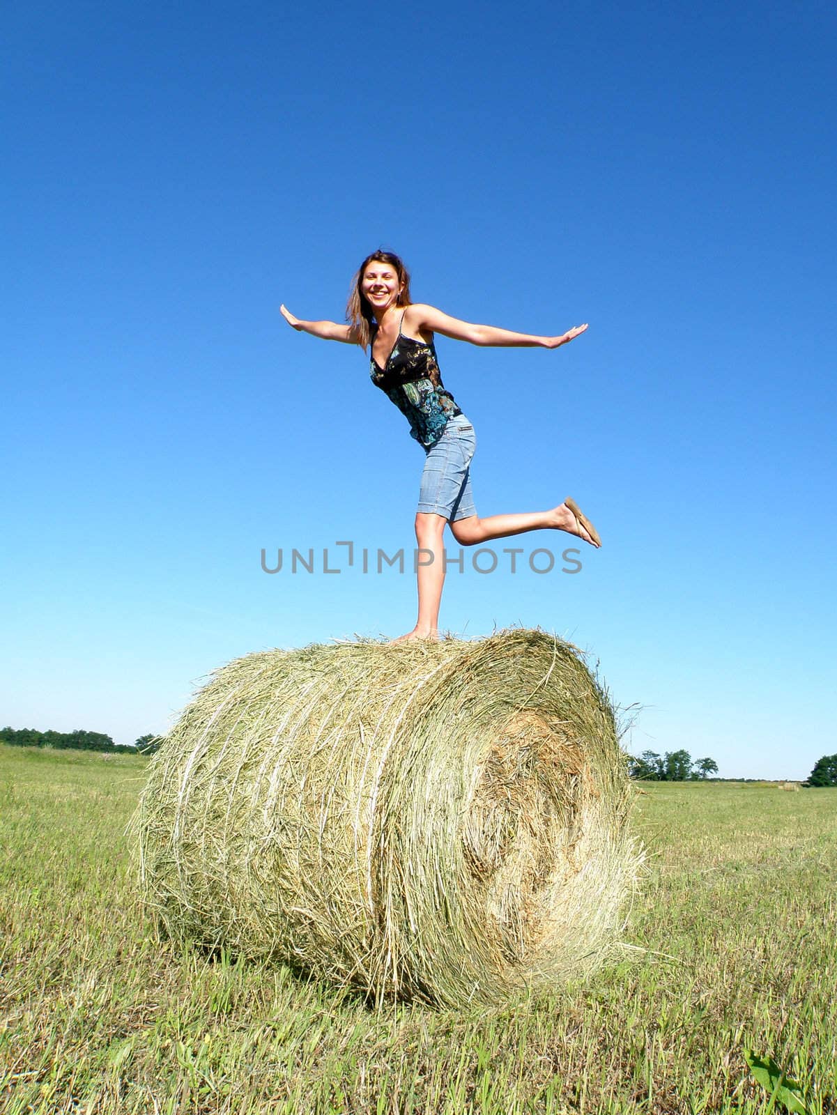 young girl costs on one foot on a hank of yellow hay    