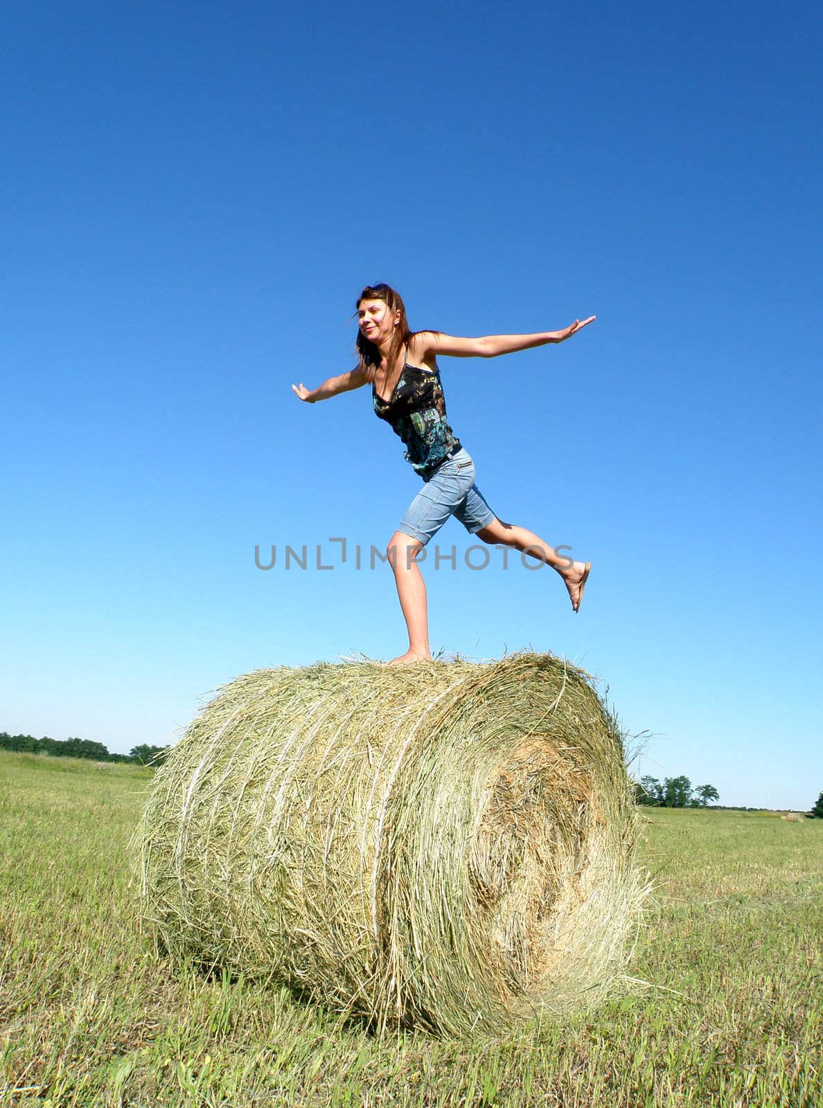 young girl costs on one foot on a hank of yellow hay