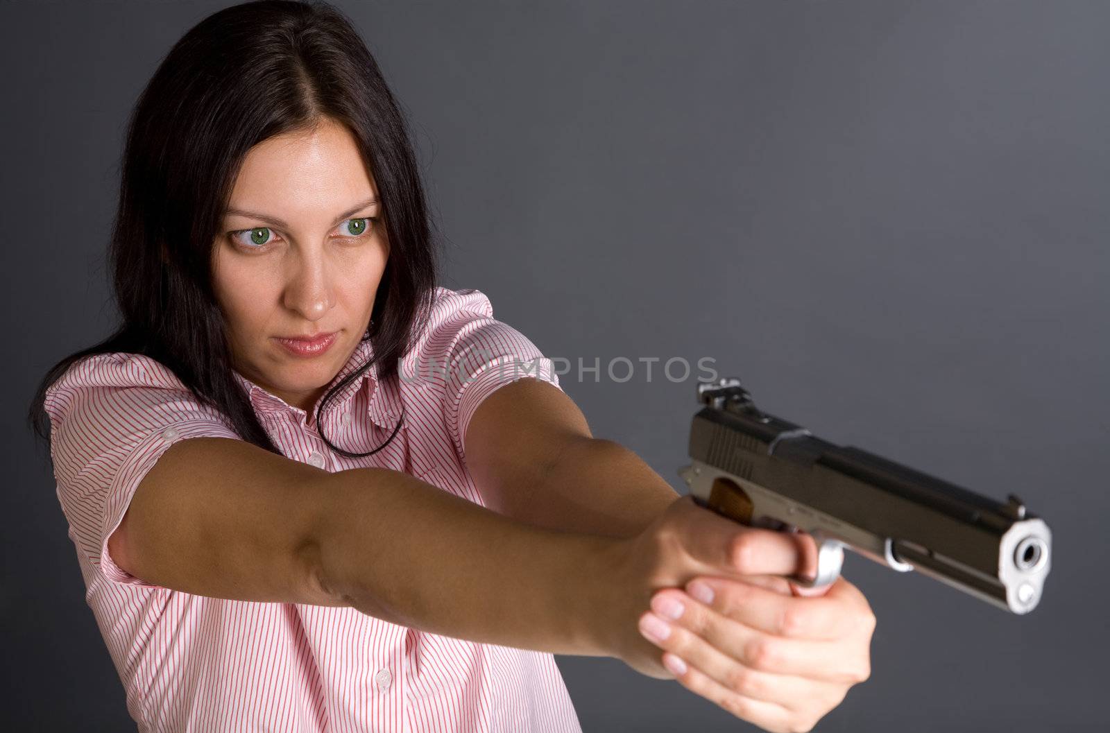 Pretty caucasian girl with gun aiming to somebody over gray