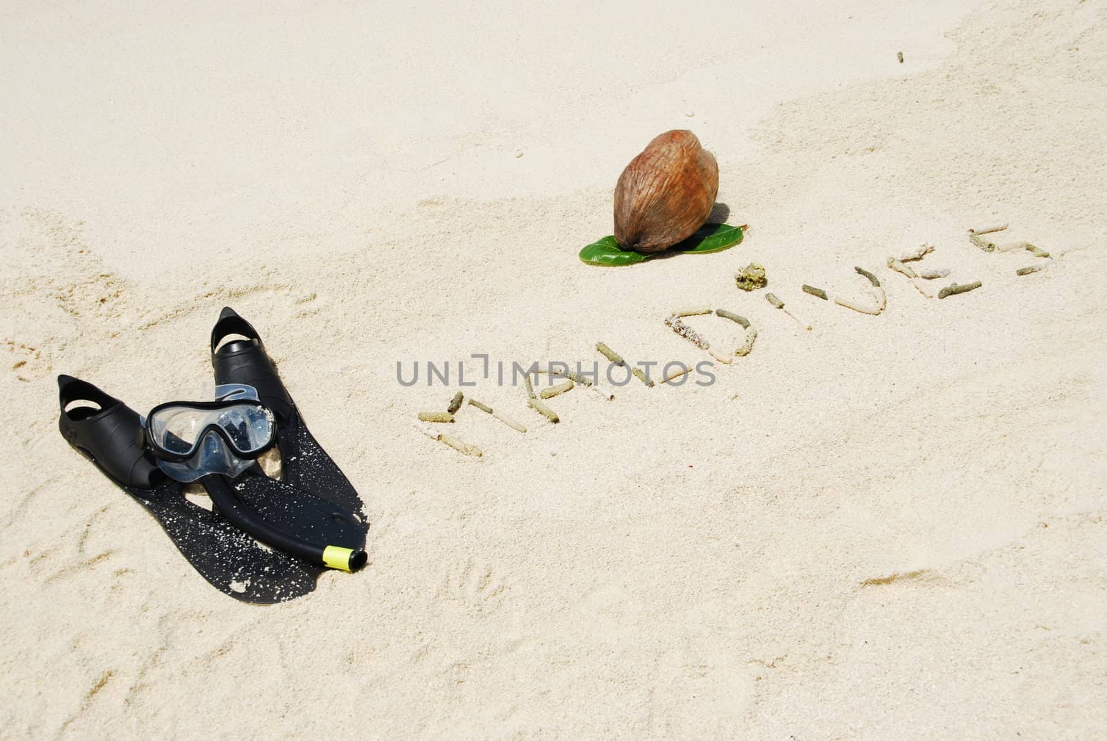 Maldives written in a sandy beach with coconut and snorkeling equipment