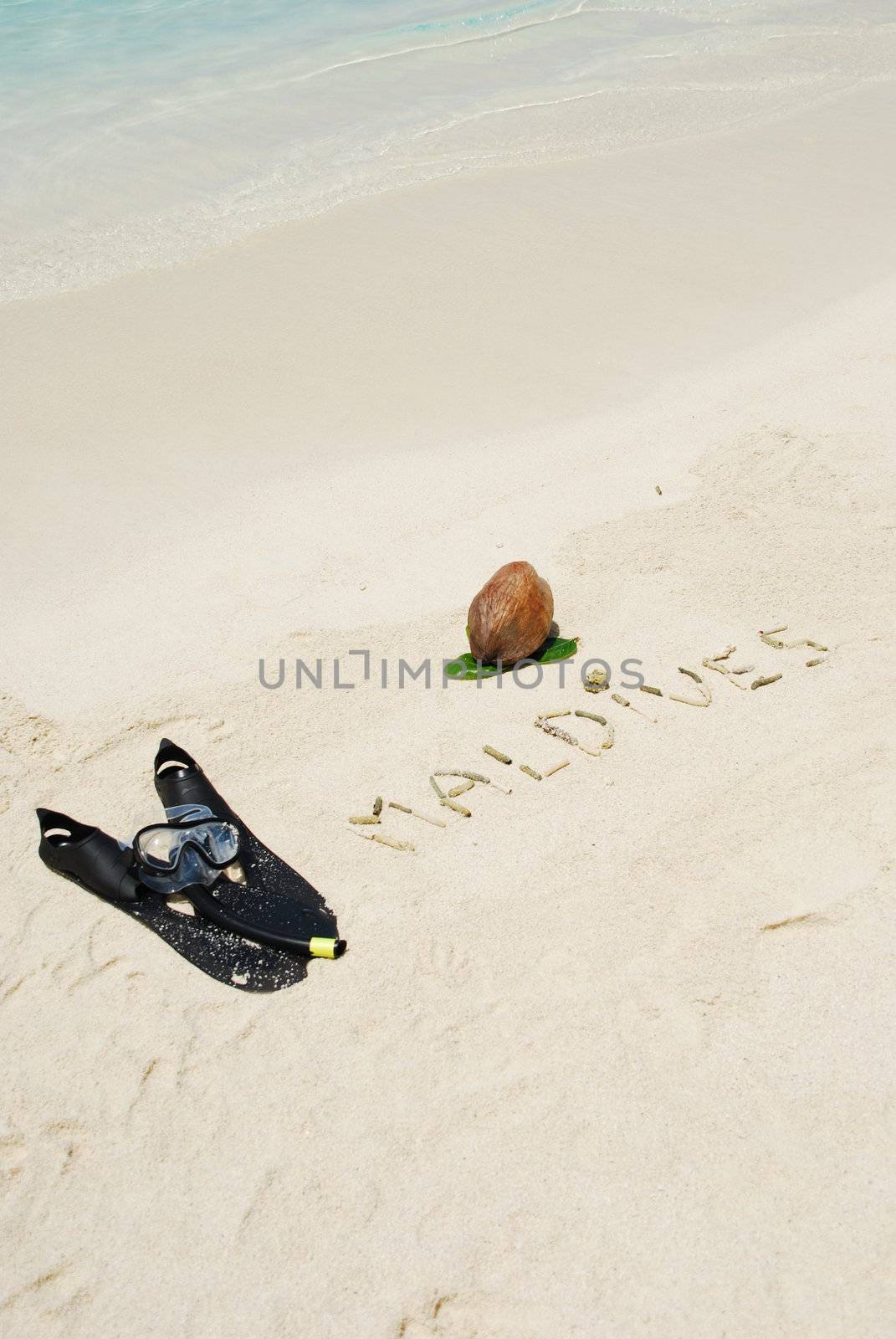 Maldives written in a sandy beach with coconut and snorkeling equipment