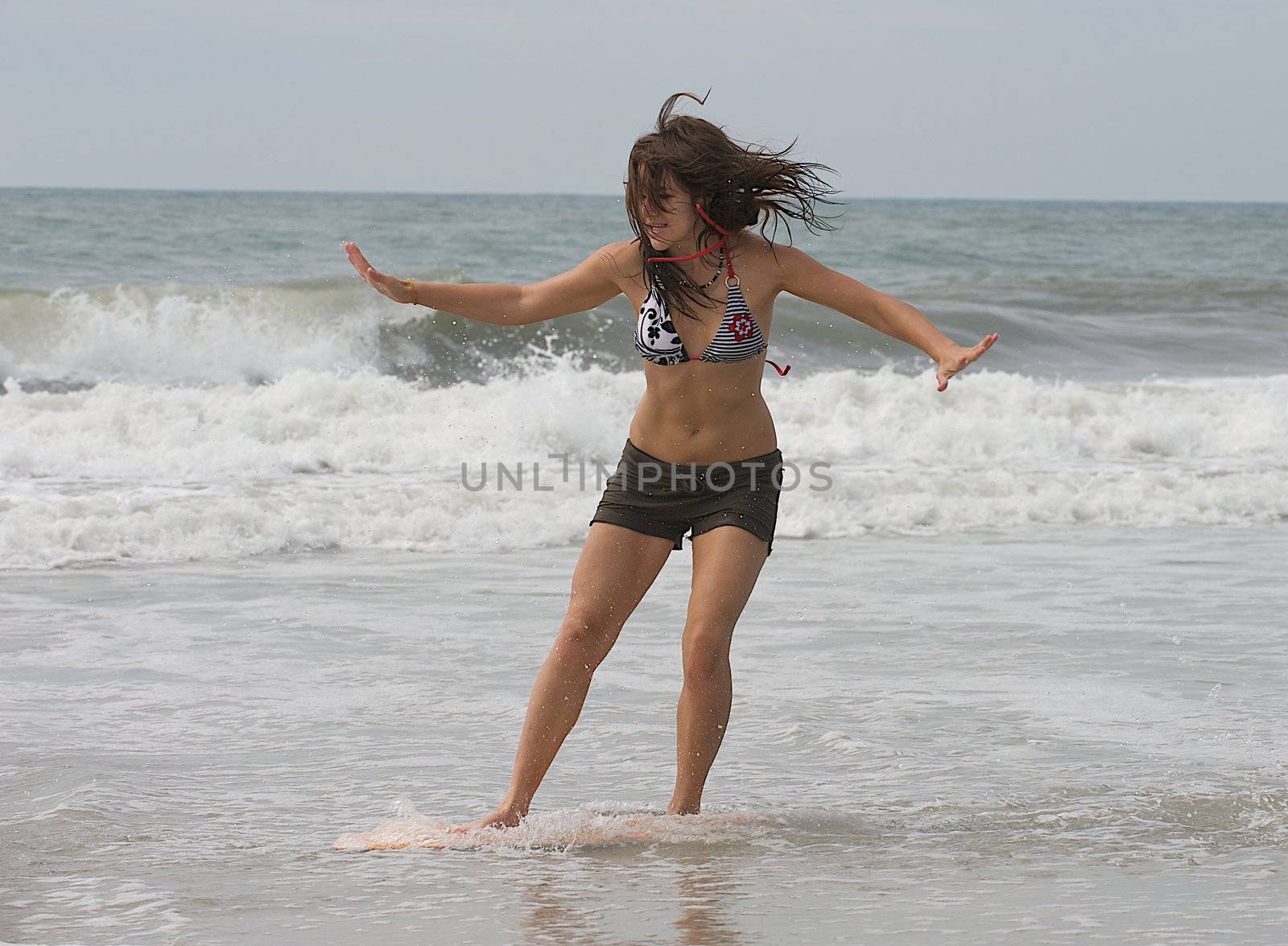 Athletic teen girl skim boarding in the surf of the Atlantic Ocean in Emerald Isle, North Carolina. 