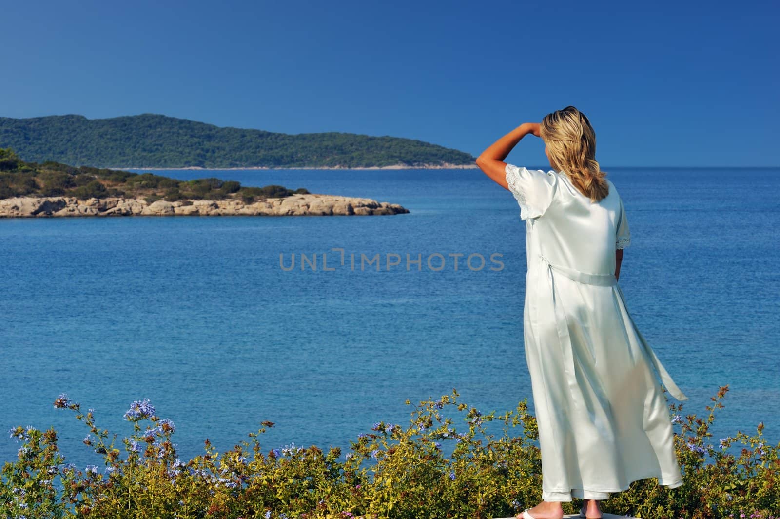 A blond beautiful woman is gazing at the spectacular view of the Greek islands during a clear morning of her summer holidays