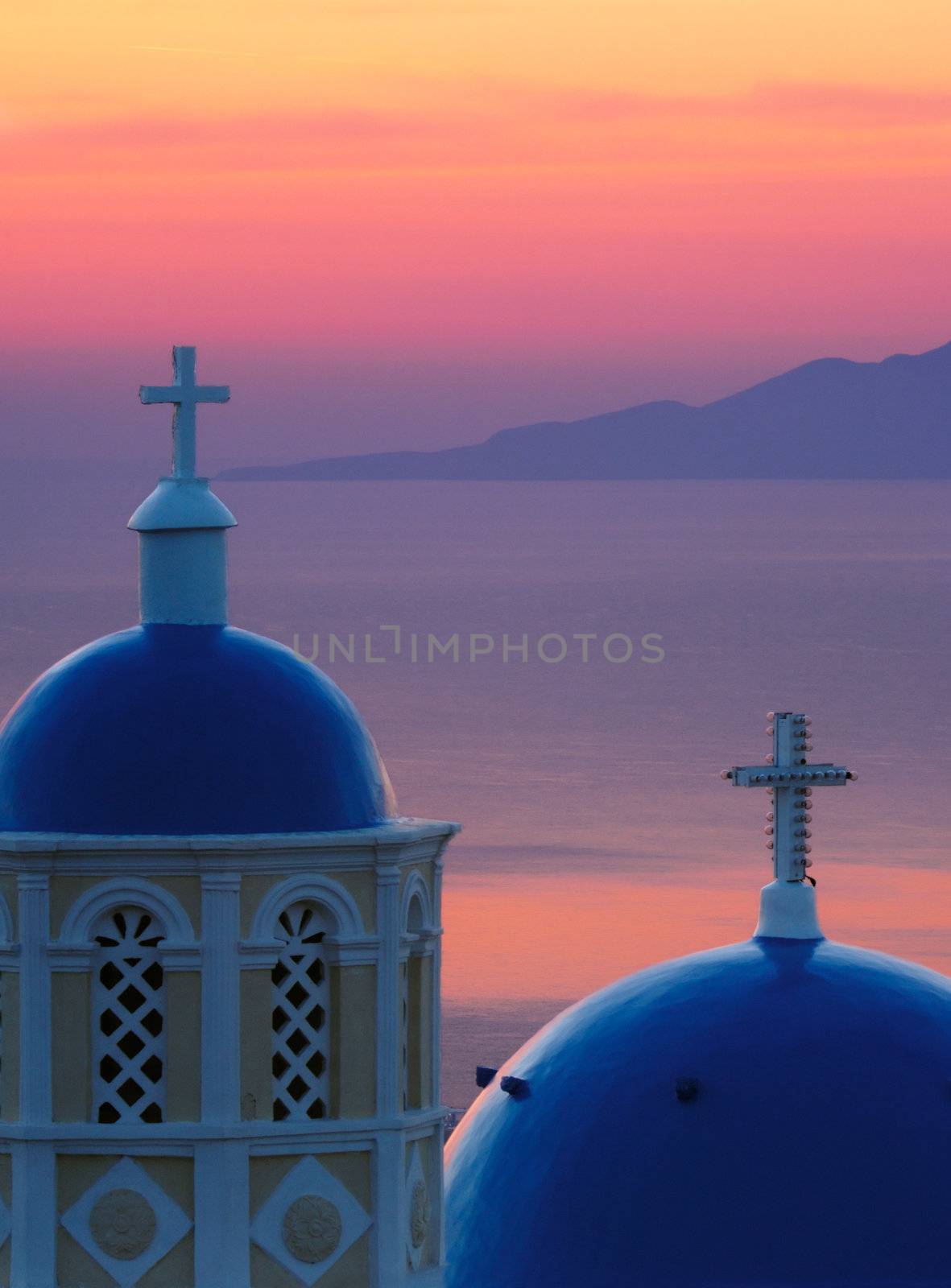 Image shows two church domes, typical of Santorini, against the Aegean Sea, washed in pre-sunrise colors