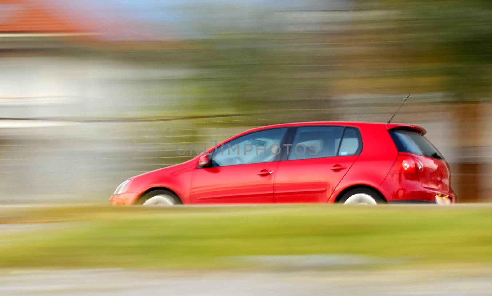 This is a panning shot of a fast moving red small car