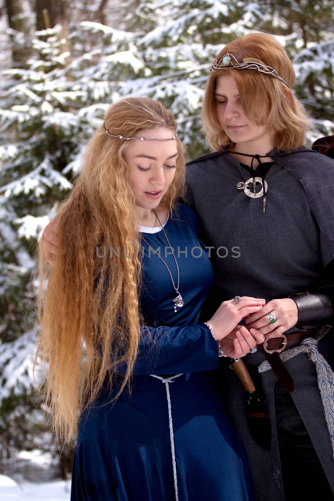Two ladies in medieval dresses in winter forest
