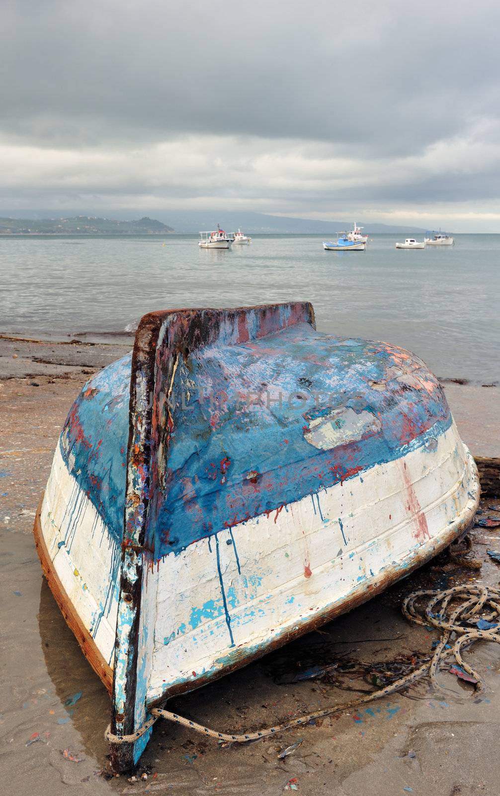 Picture from a fishing village showing an upside down and heavily weathered fishing boat stranded on the beach. Room for text on top. 