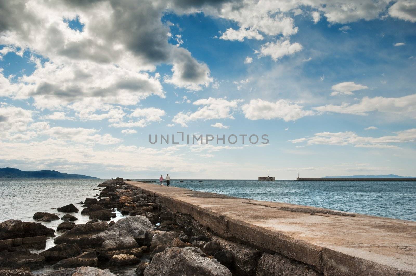 A couple in the distance strolling along the pier in Kalamata, southern Greece, under a spectacular cloudscape