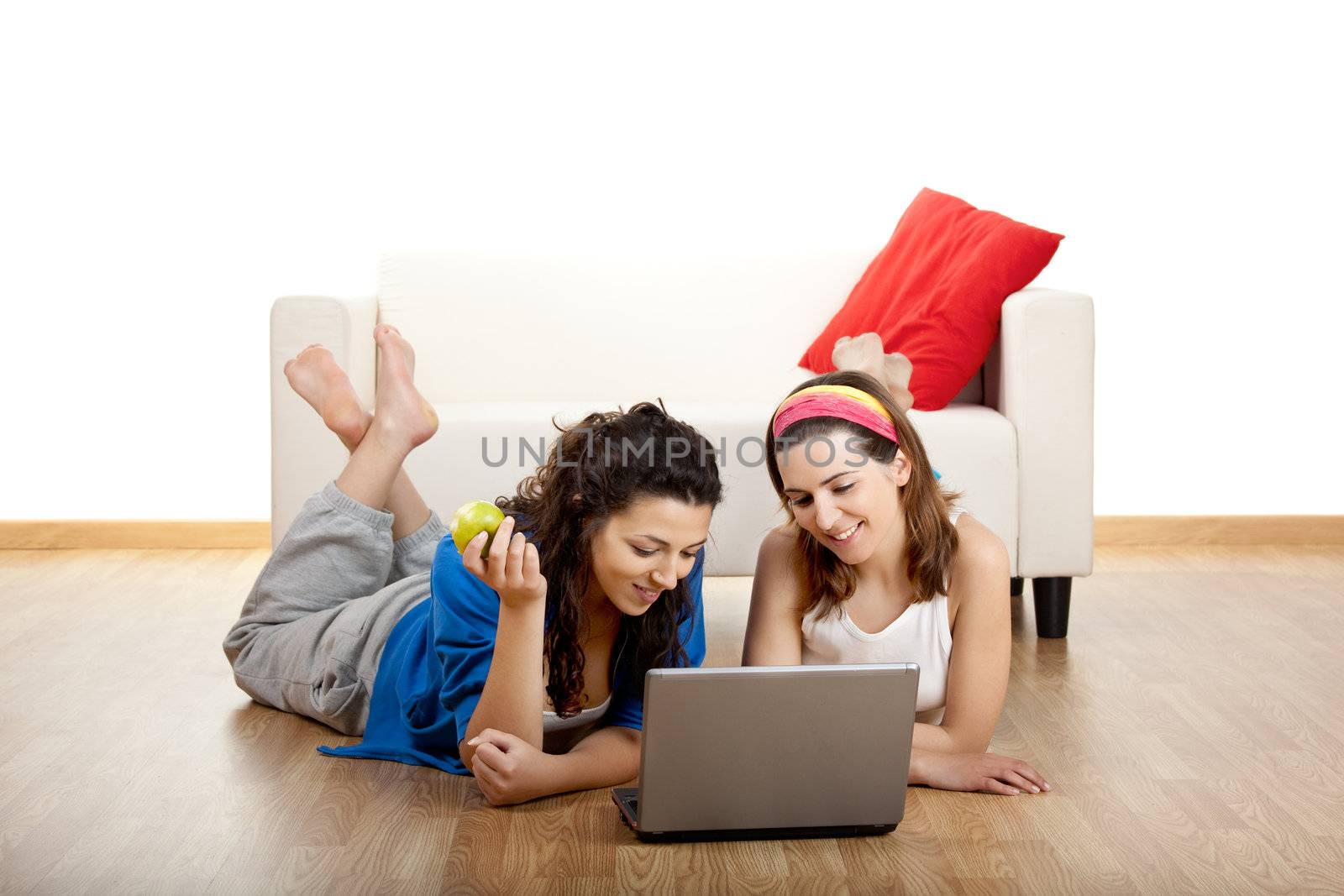 Two beautiful young women sitting on floor working with a laptop