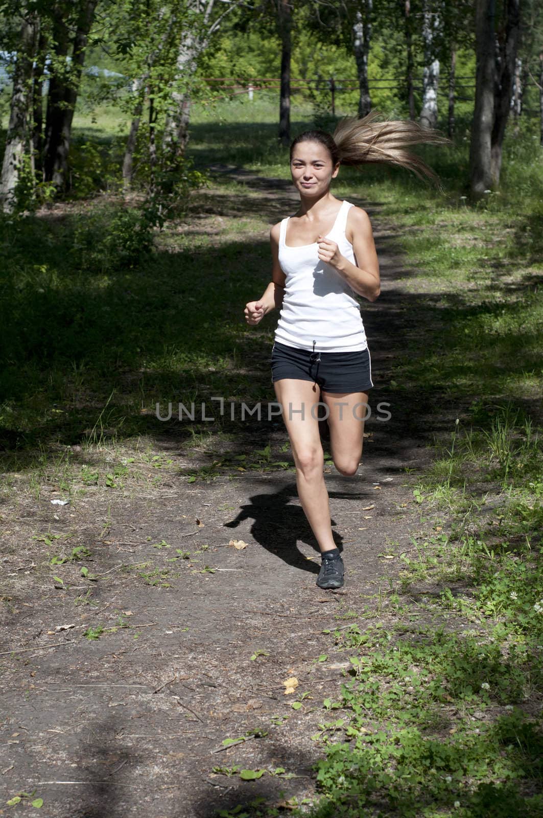 young woman jogging in the park in summer, trees and grass background