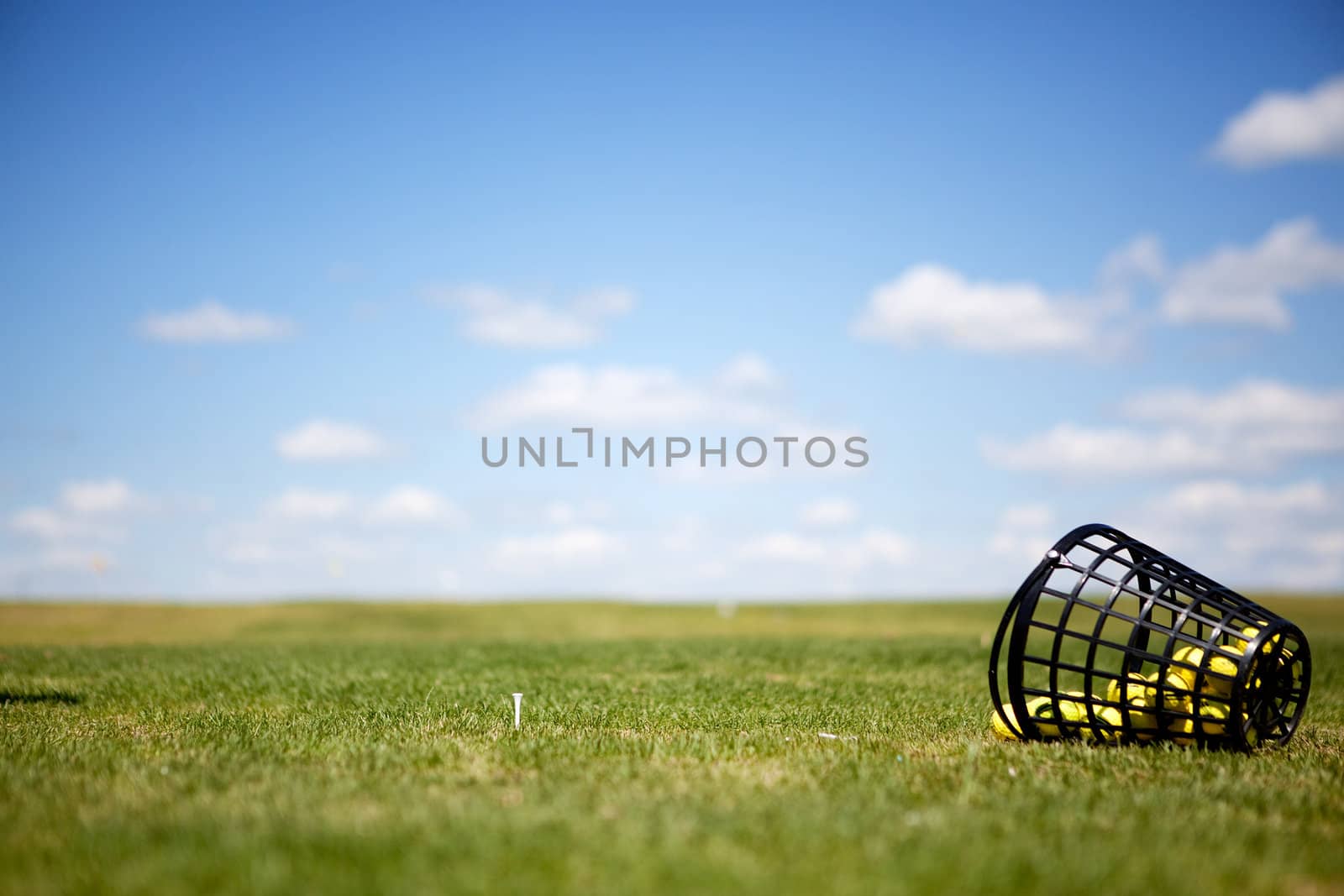 A tee and yellow golf balls on a driving range