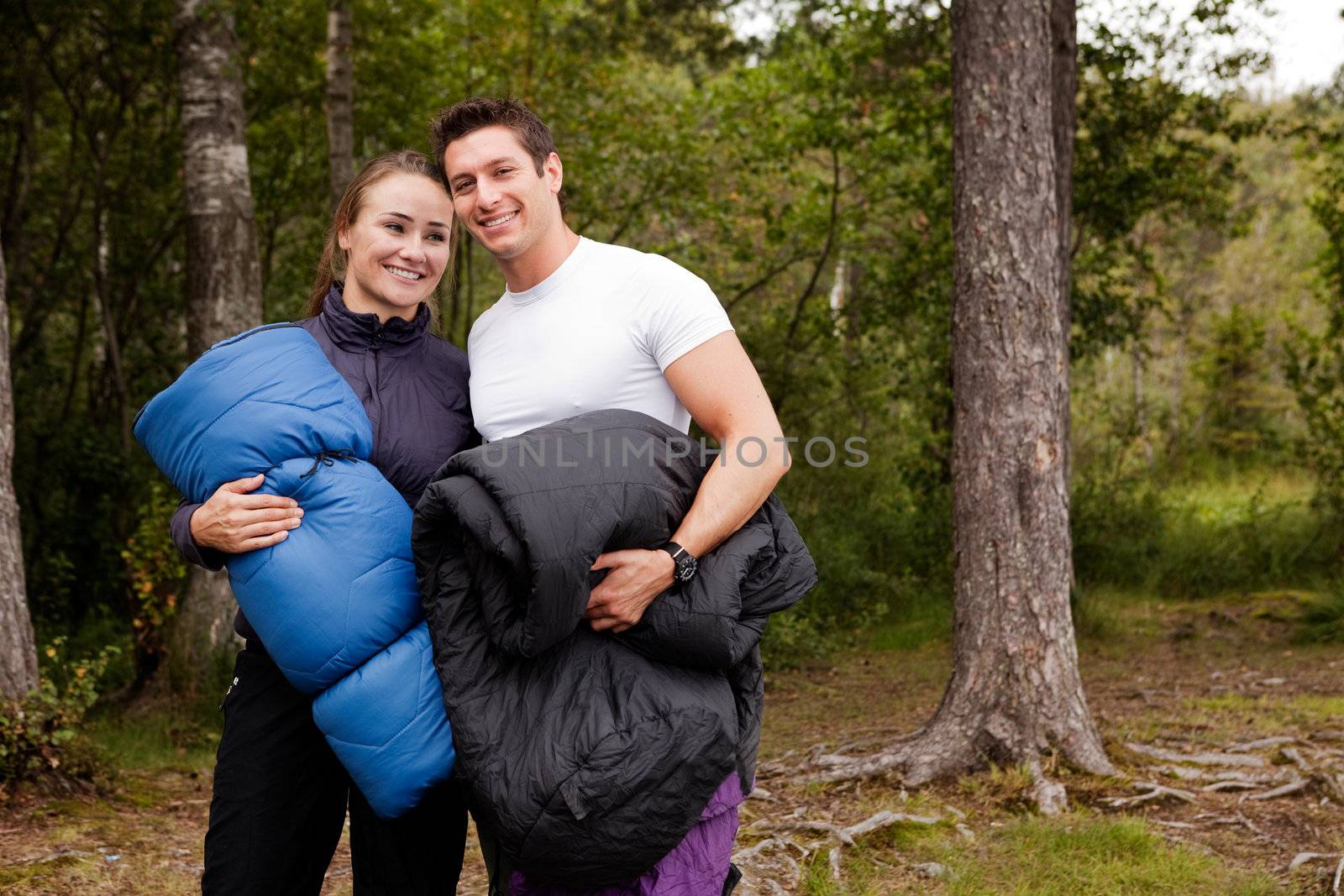 A couple of happy campers standing with sleeping bags