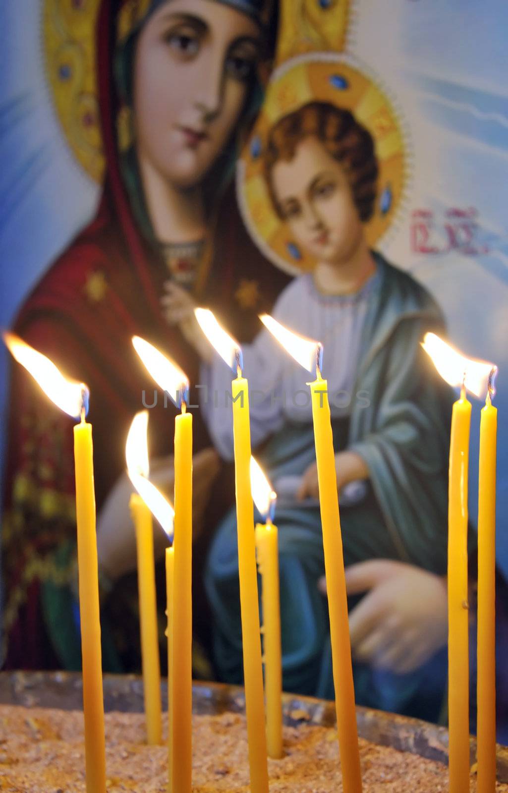Lit candles in a Christian Orthodox church, with an an icon of Virgin Mary and Jesus in the background