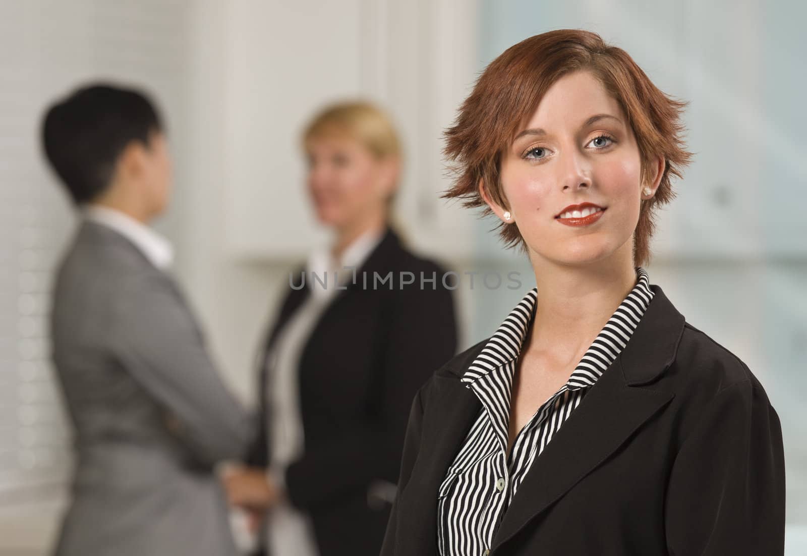 Pretty Red Haired Businesswoman with Colleagues Behind in an Office Setting.