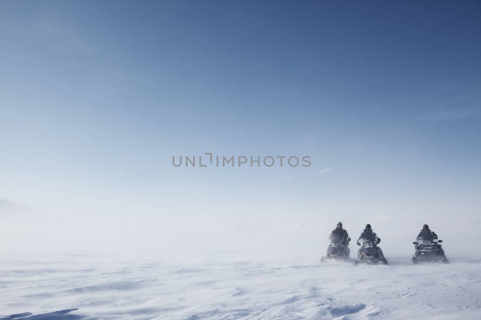 Three snowmobiles on a blowing barren winter landscape