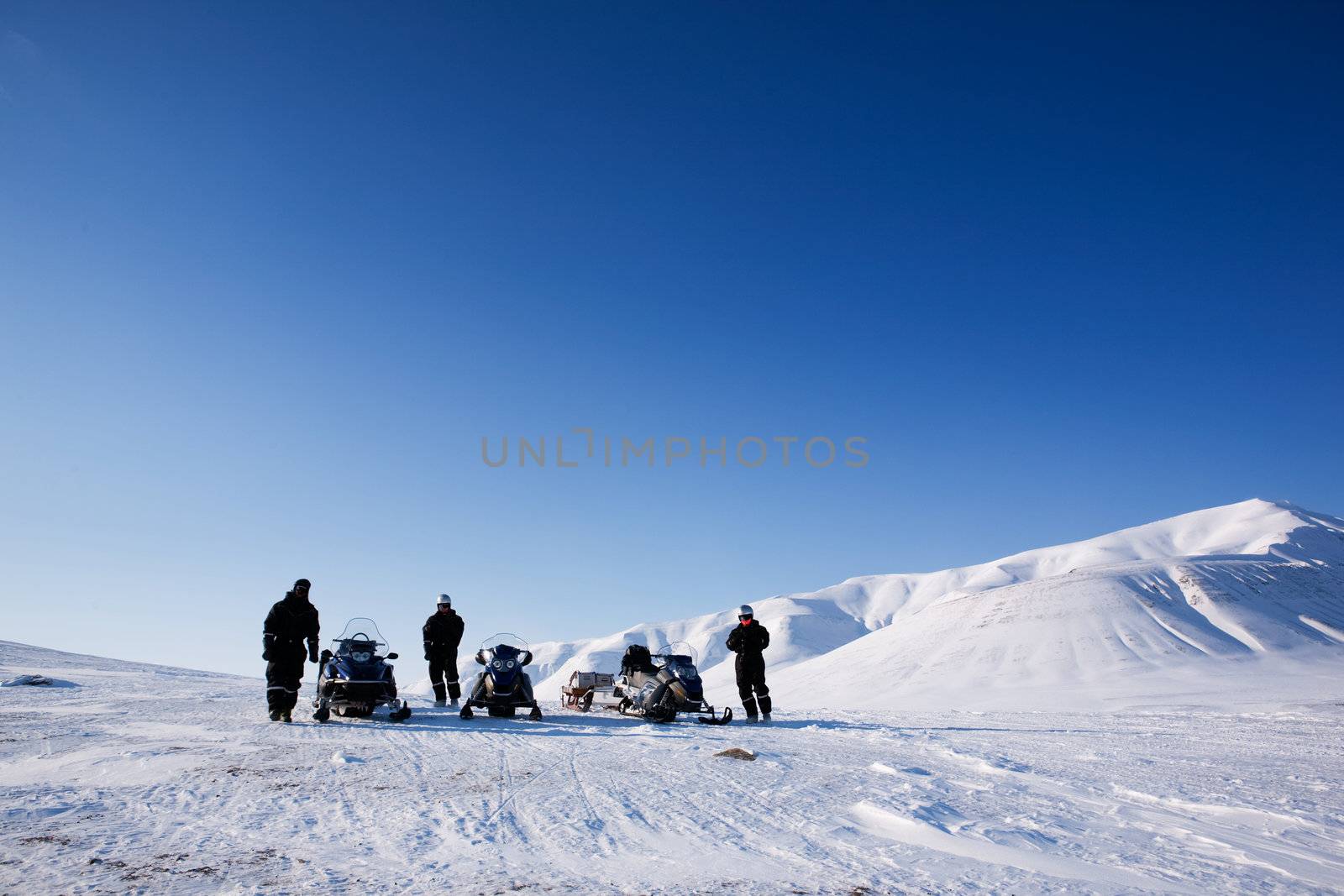 Three people with snowmobiles in an arctic landscape