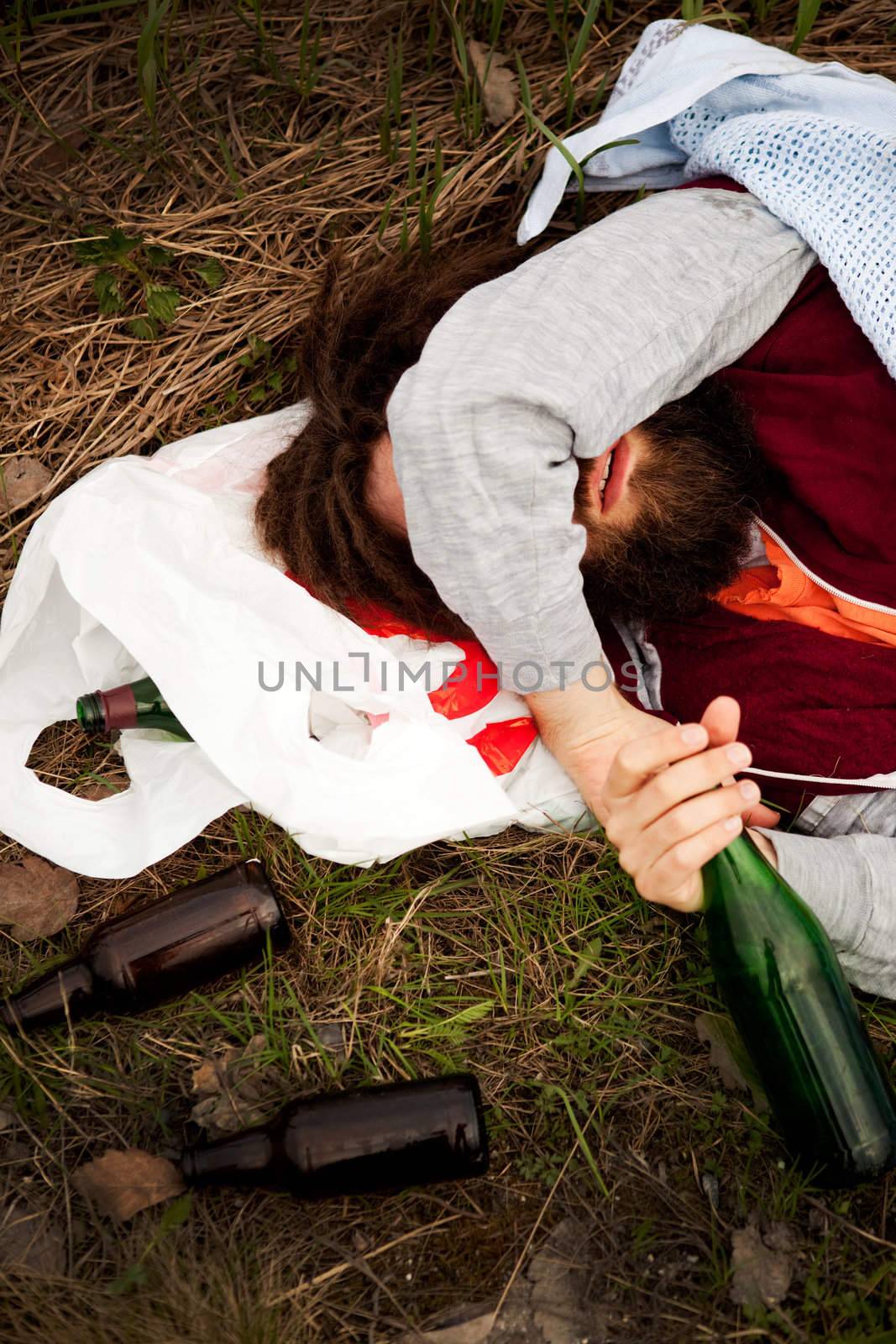 A drunk person sitting in a ditch with a wine bottle