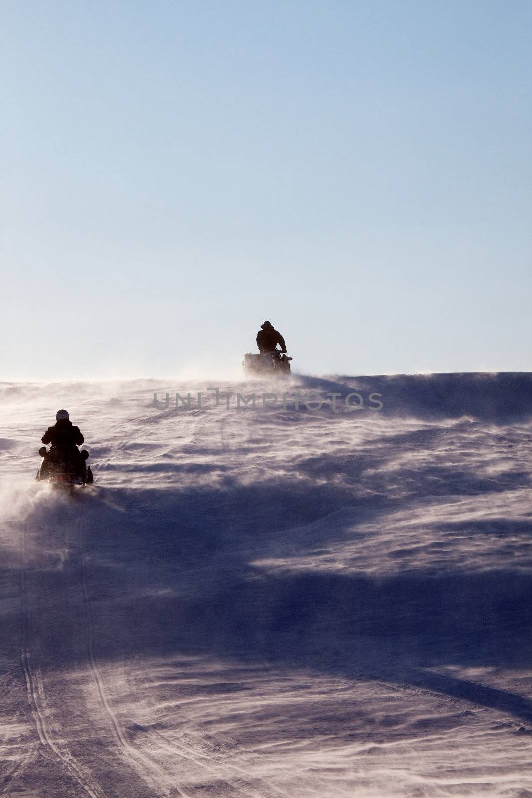 Two snowmobiles driving up a hill in a snow storm