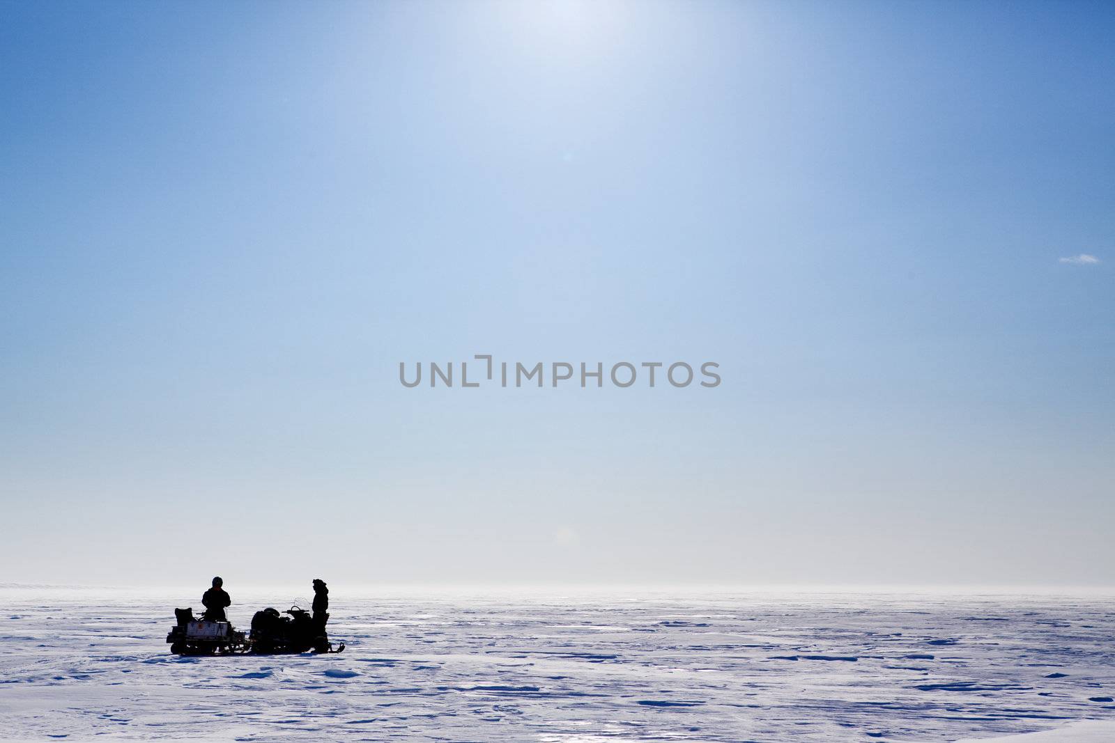A barren flat winter landscape with two people and snowmobiles