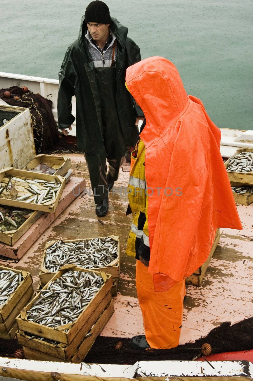 Picture shows two fishermen on a trawler boat in a rainy winter day