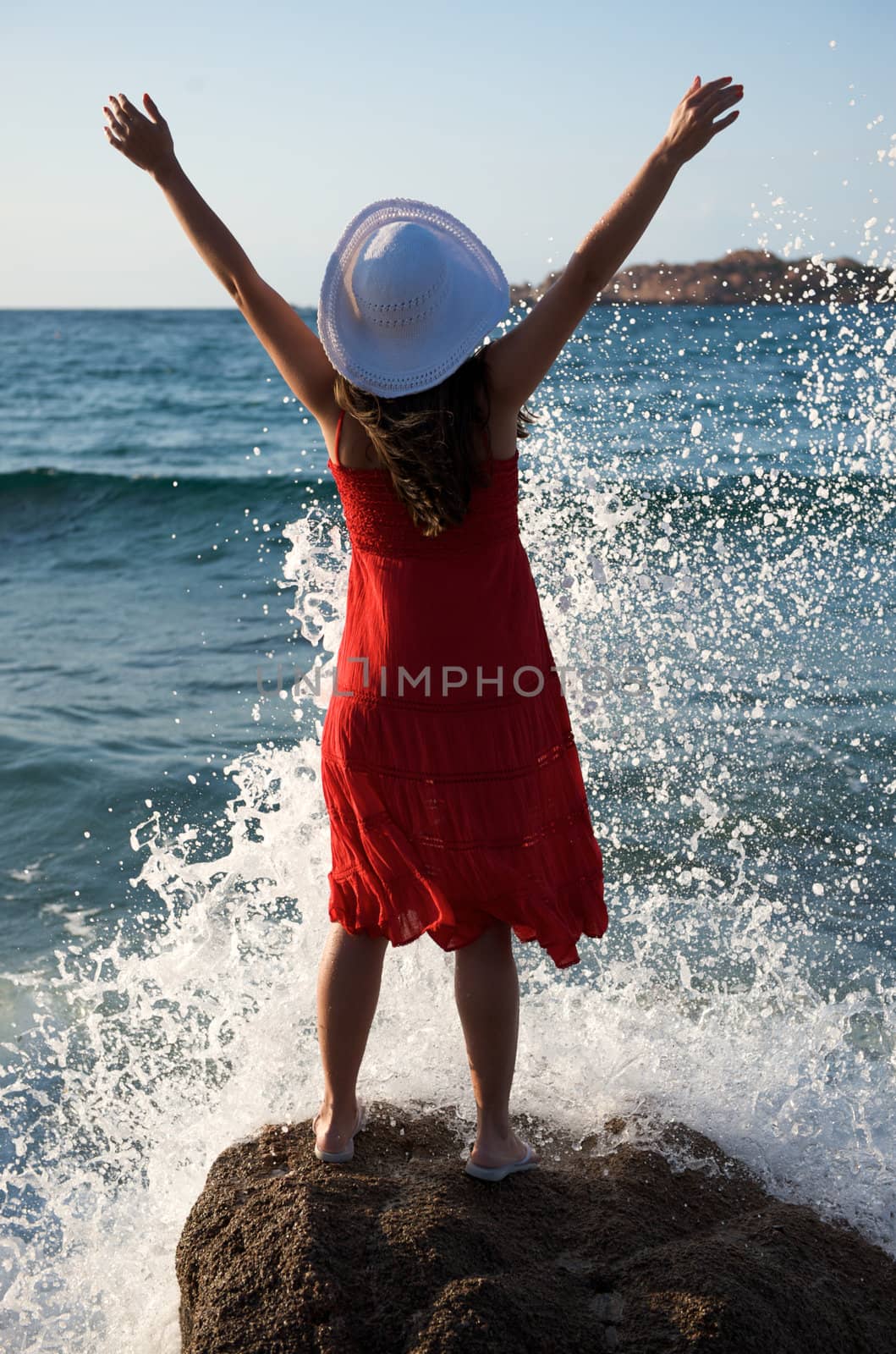 Pretty girl splashing by the wave on the beach at sunset time