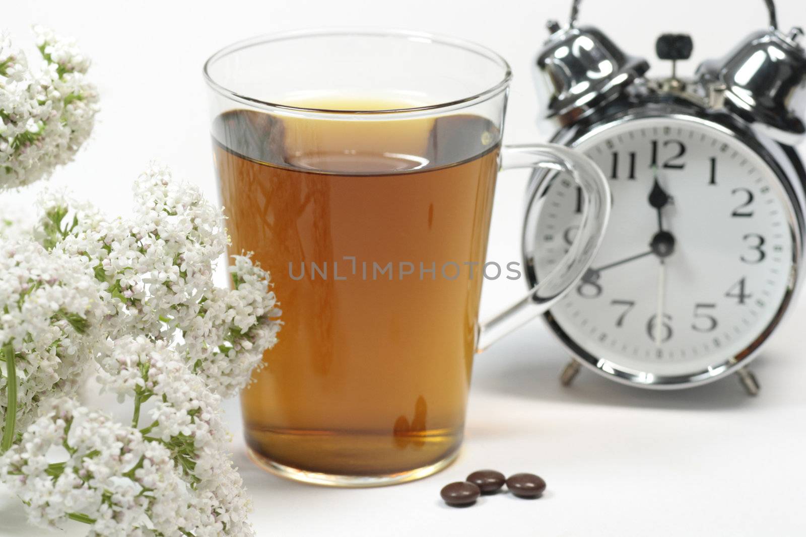 Cup of herbal tea, brown pills, valerian and alarm clock over white background