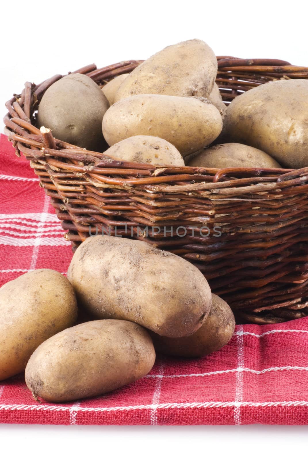 Basket full of potatoes with knife, standing on cloth, isolated on white.