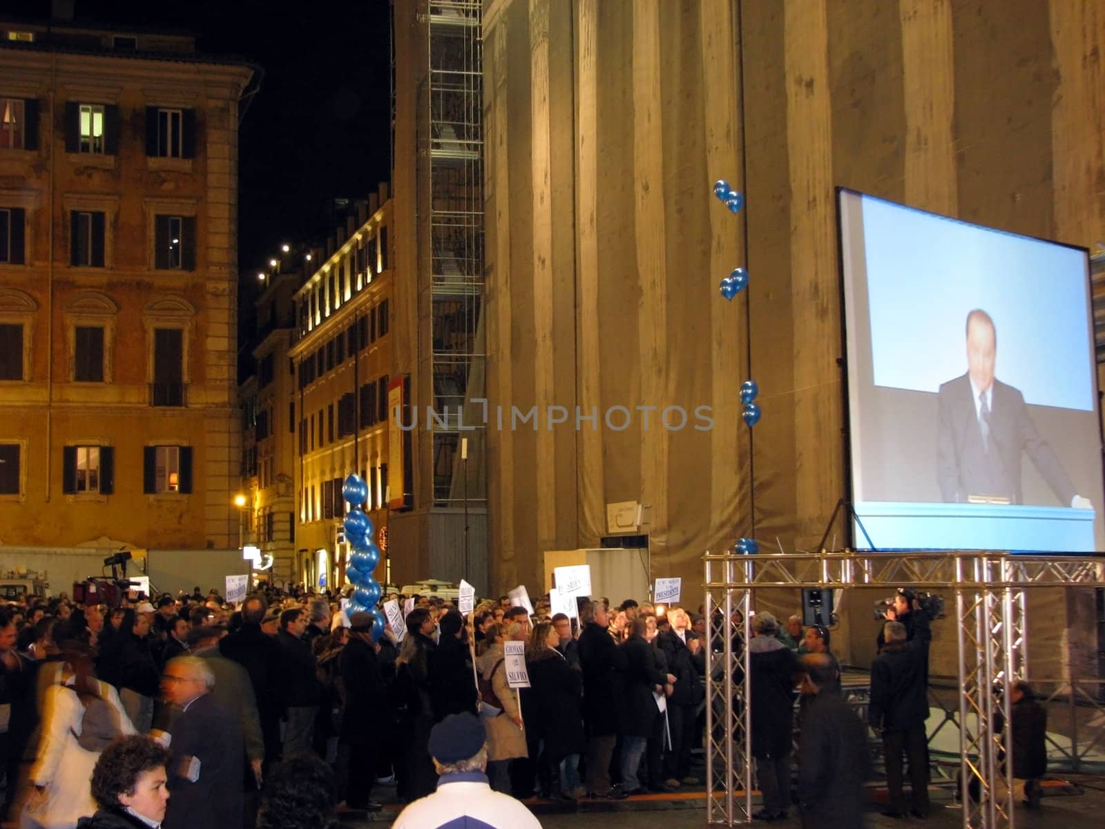 A night time political rally takes place in Rome, Italy. President Silvio is projected on the screen outside. He was speaking inside the building behind the screen.
