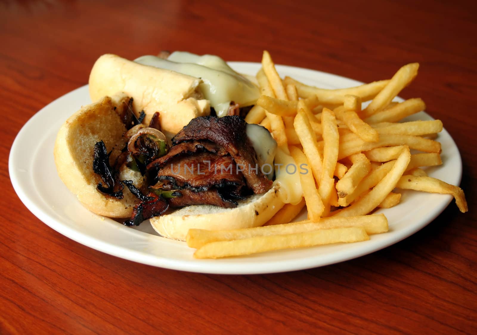 cheese steak with french fries on white plate and wood background
