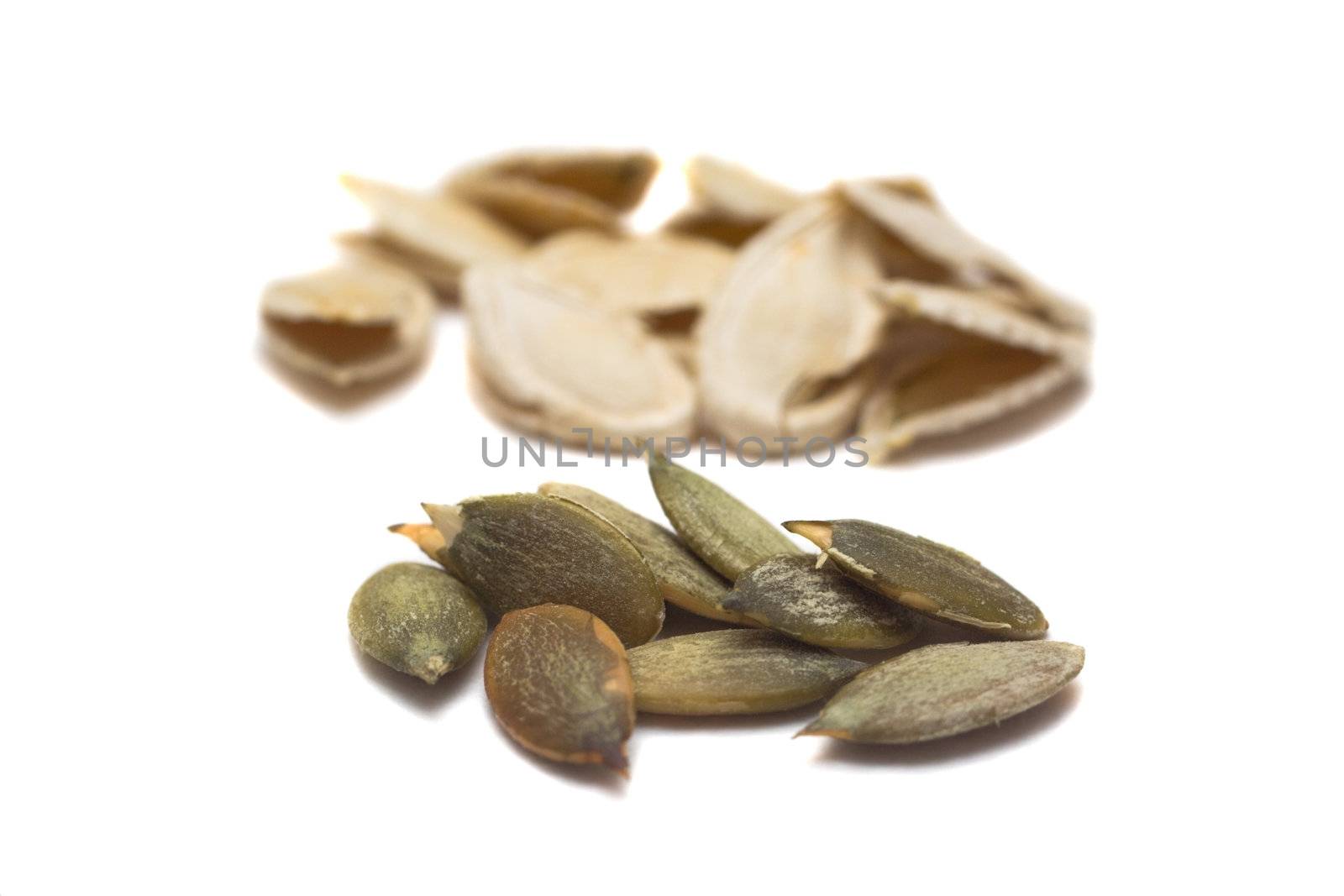 peel pumpkin seeds on focus and shells behind them, isolated on white