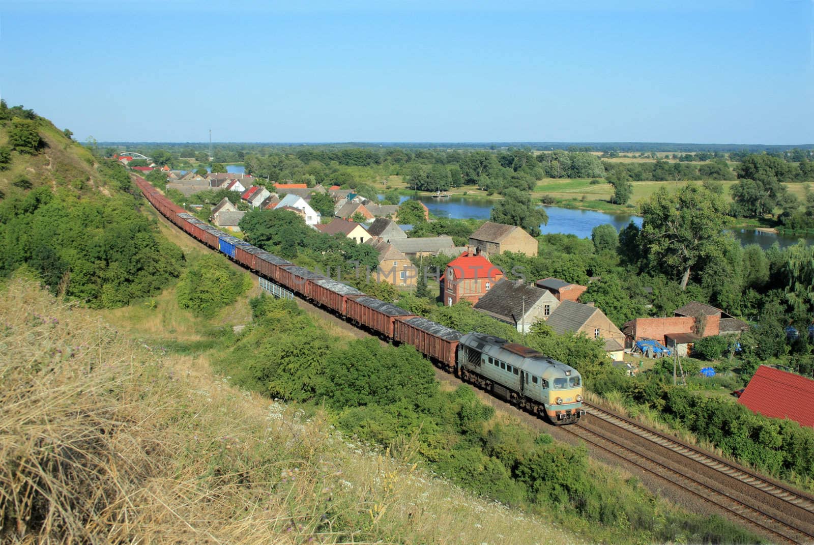 Freight train passing the village with the river in background
