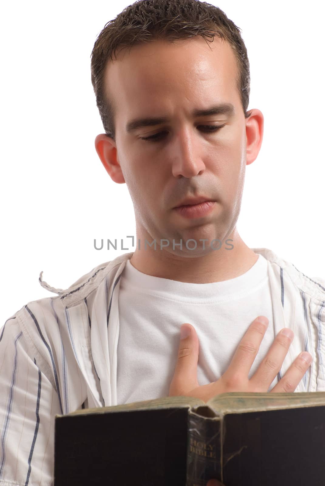 A religious man is reading an old bible while holding one hand over his heart, isolated against a white background