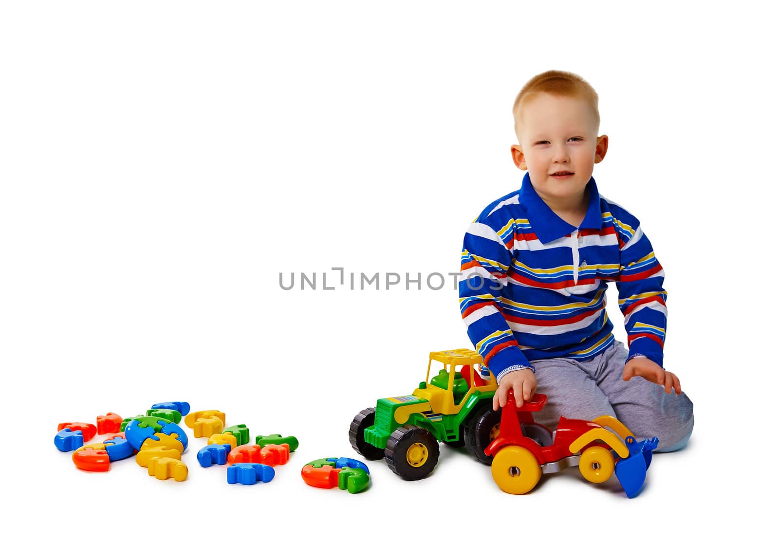 A little boy sits on a white background with toys
